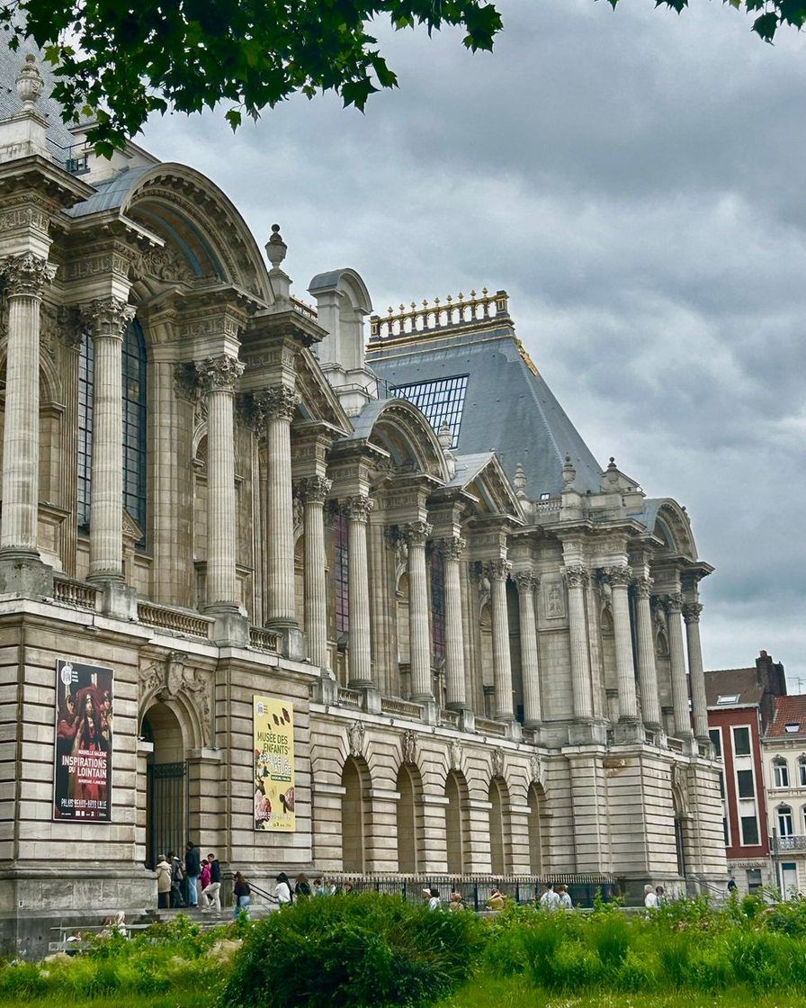 Façade de pierre claire du Palais des Beaux-Arts de Lille avec ses hautes fenêtres cintrées, bassin d'eau au premier plan reflétant le bâtiment, place déserte le matin